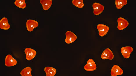 Overhead-Shot-Of-Romantic-Lit-Heart-Shaped-Red-Candles-Revolving-On-Black-Background-Flickering